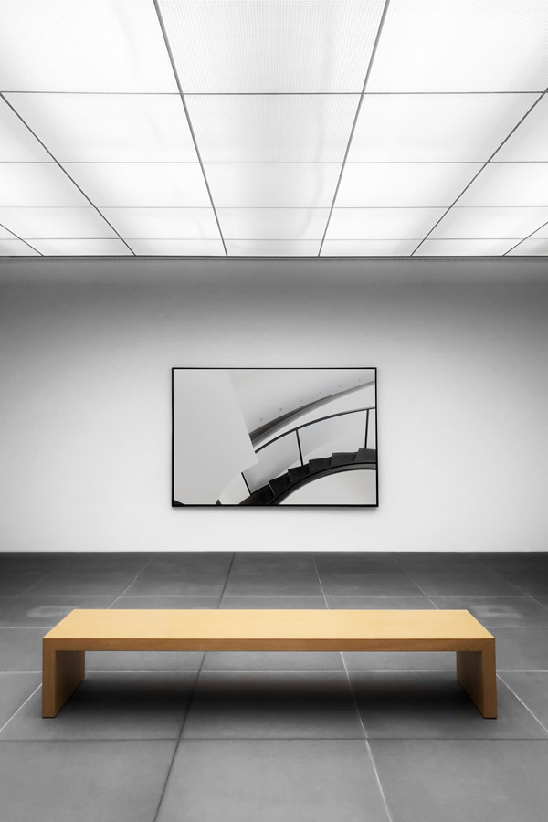 A quiet gallery with a wooden bench and framed architectural photograph