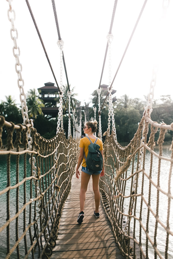 A traveler standing on a suspension bridge surrounded by greenery