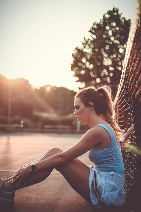 A woman seated beside a tennis court in warm evening light